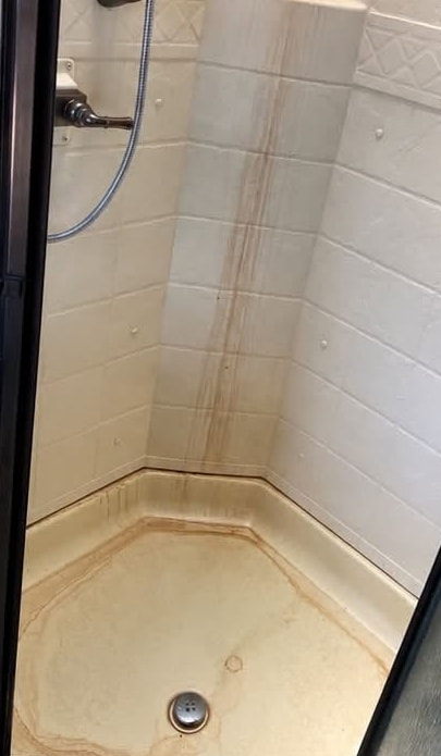 A shower before cleaning, with rust-colored streaks running down the corner and stains across the shower pan